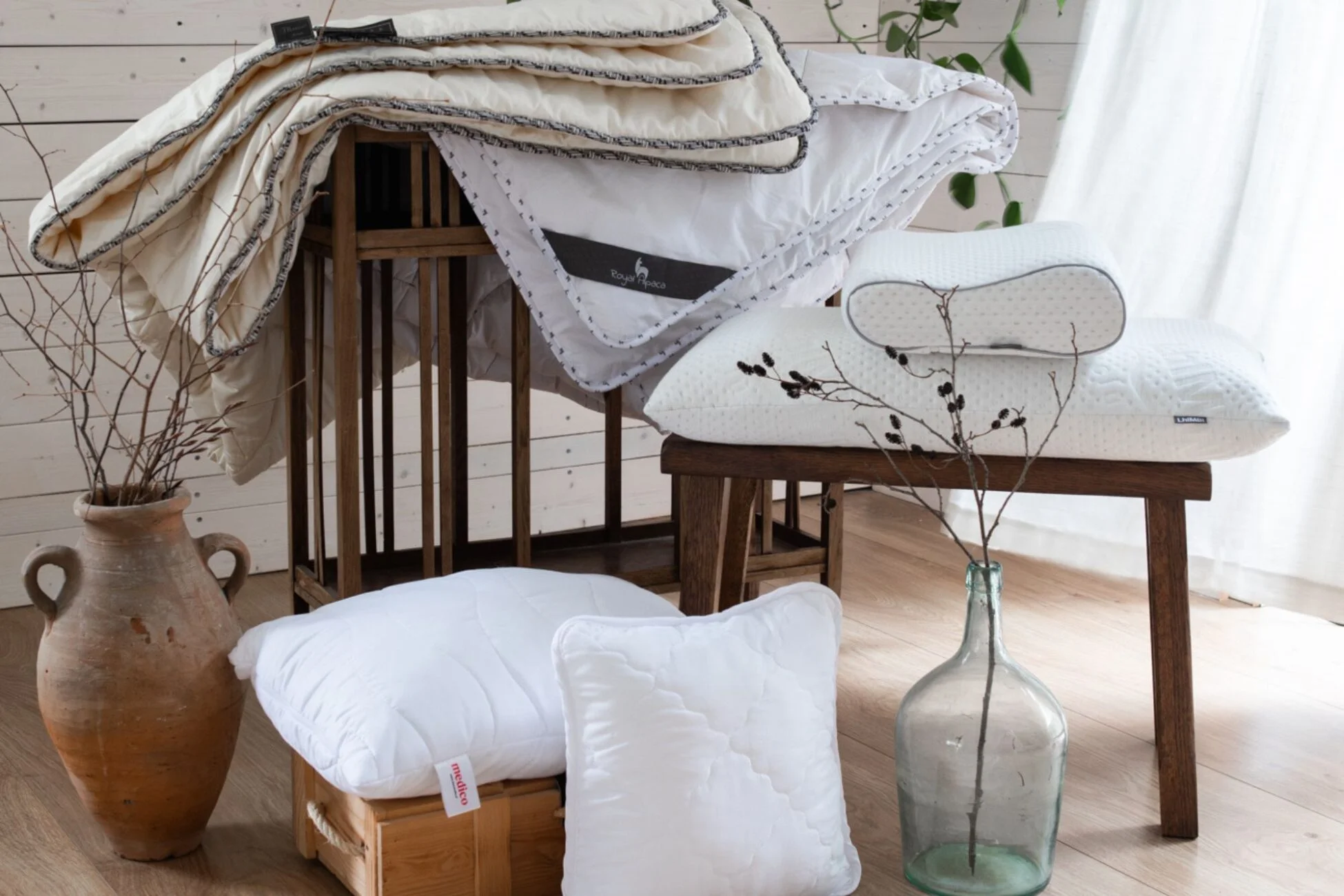 Kołdry i poduszki eurowolle na drewnianych stołku i stoliku,