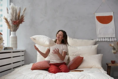 Kobieta siedząca na łóżku. Podrzuca poduszkę merino line