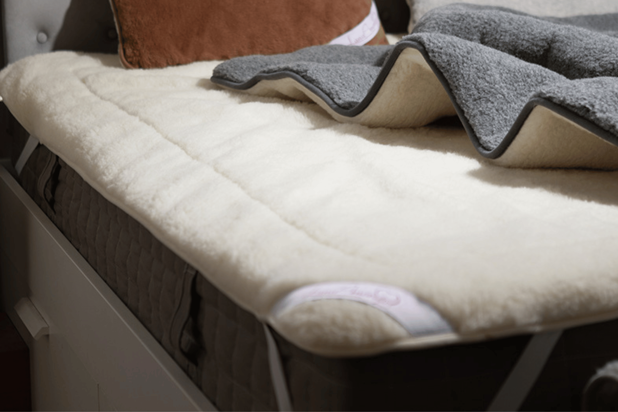 wełniany ochraniacz na materac w kolorze kremowym na łóżku z szarym kocem i poduszką