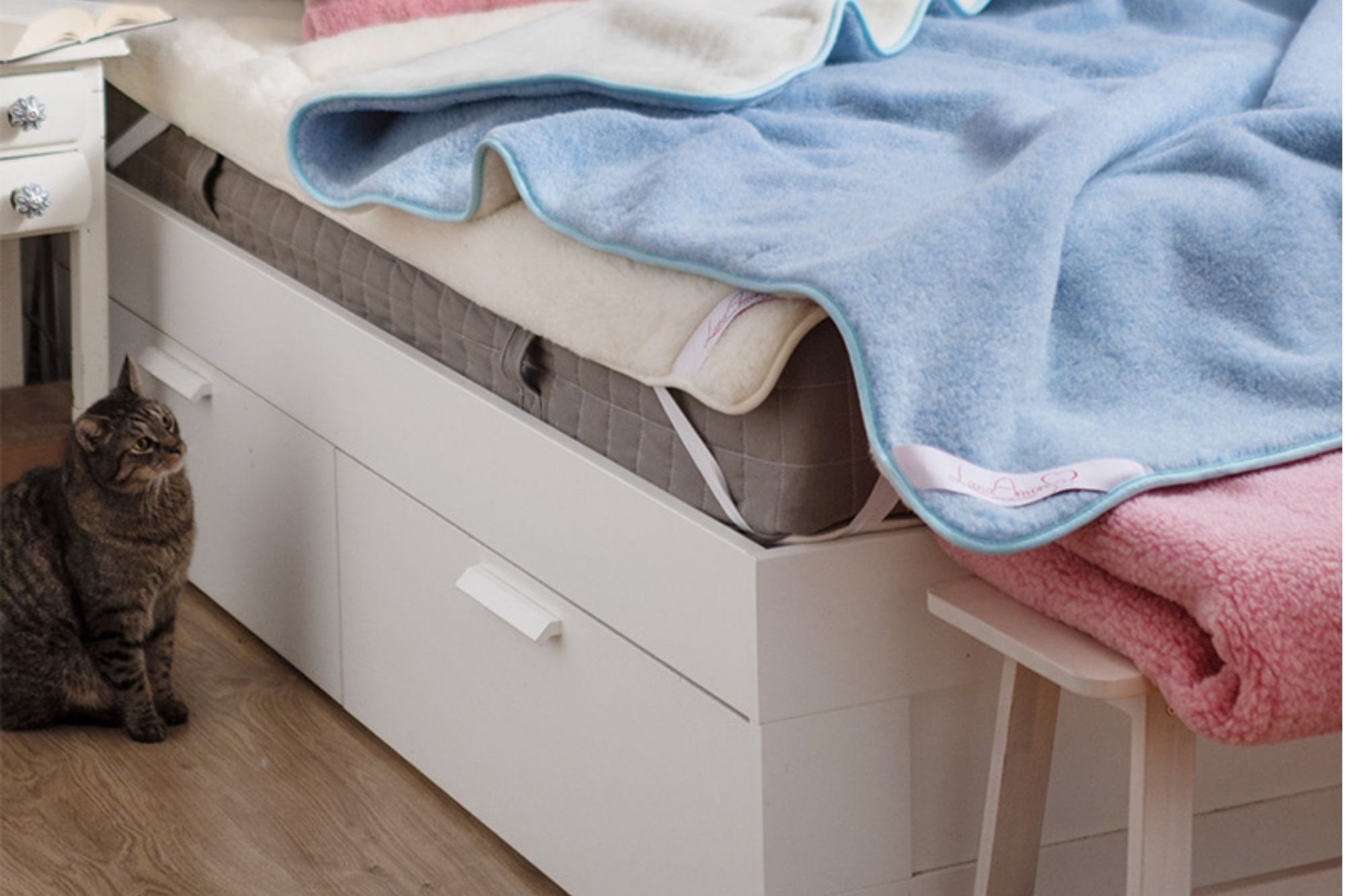 Niebieska kołdra wełniana na łóżku z białym i różowym kocem, obok siedzi kot