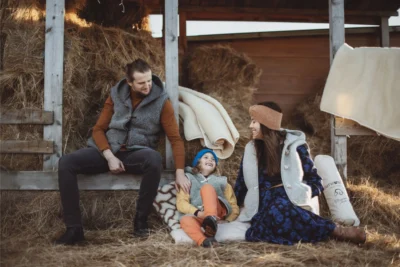 Rodzina w sielskiej scenerii. Mama, Tata i syn. Wszyscy w wełnianych kamizelkach.