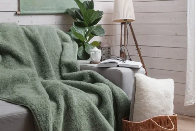 Salon. Na kanapie zielony koc wełniany. Na oparciu książka, okulary i kawa.