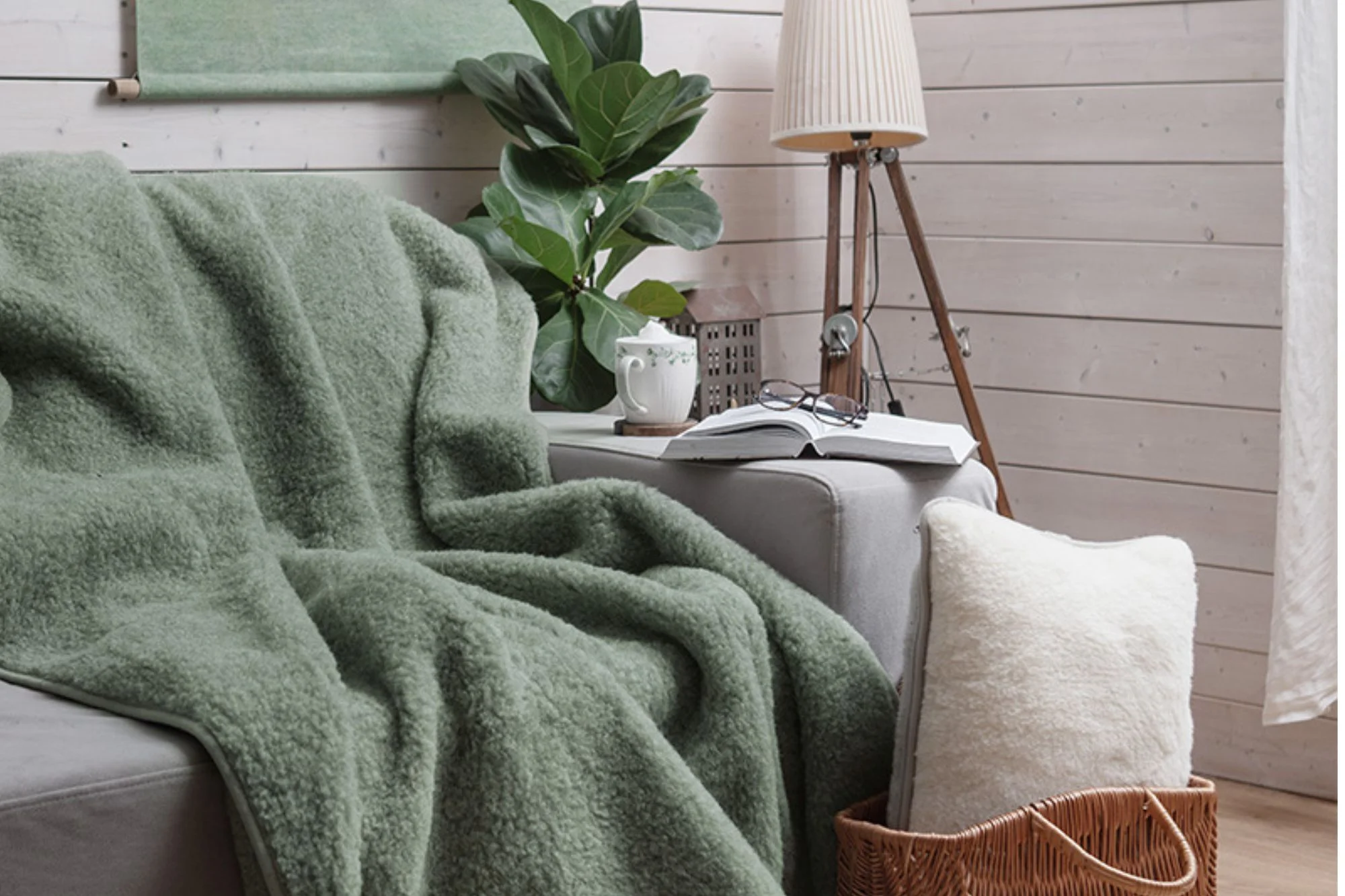 Salon. Na kanapie zielony koc wełniany. Na oparciu książka, okulary i kawa.