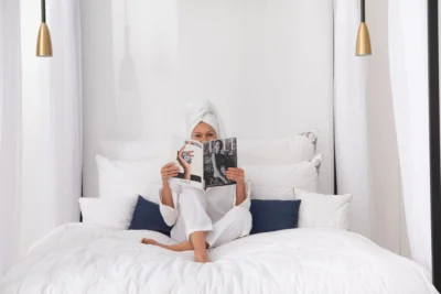 Kobieta siedząca na łóżku, czyta gazetę. Wokół niej poduszki z wełny alpaki.