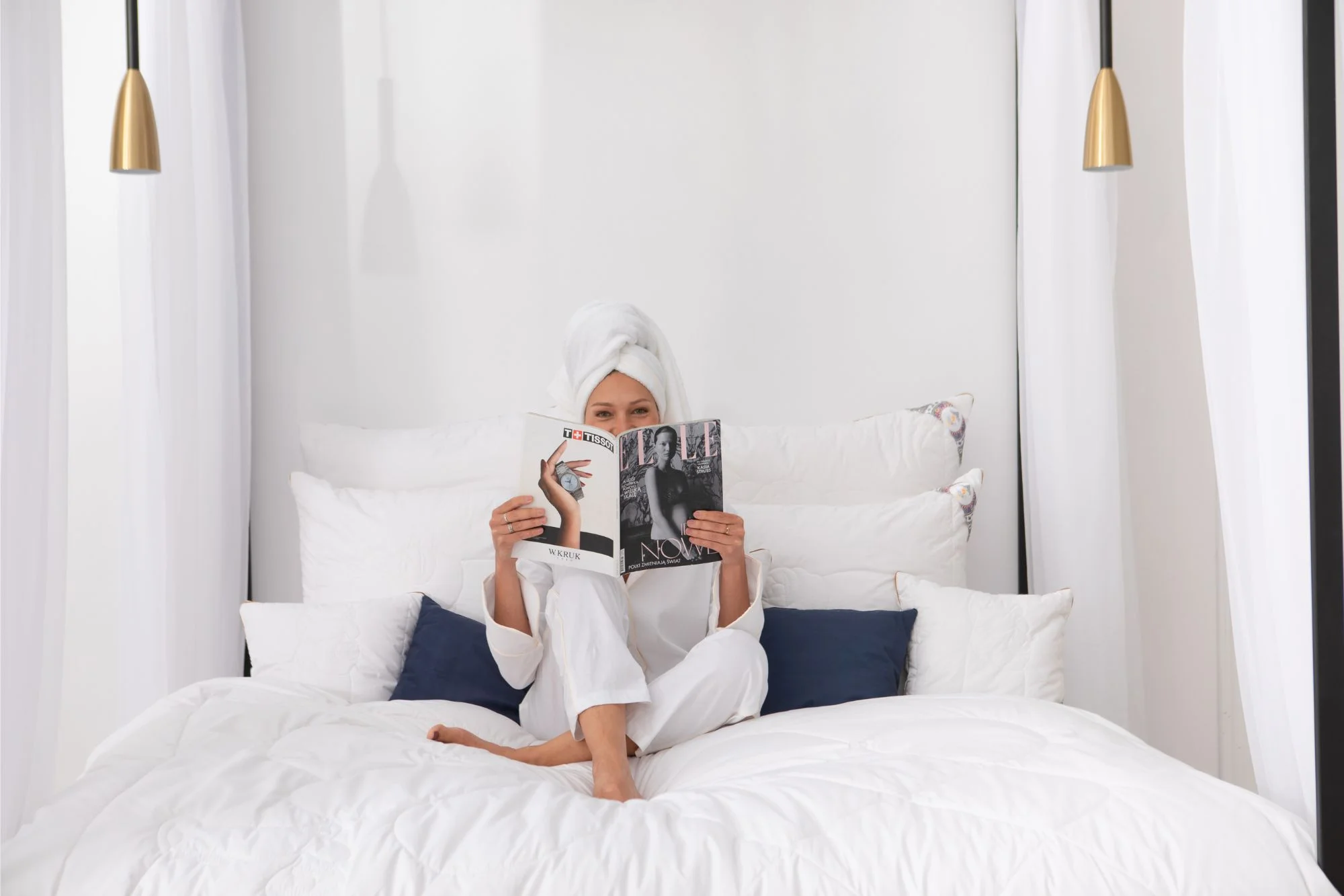 Kobieta siedząca na łóżku, czyta gazetę. Wokół niej poduszki z wełny alpaki.