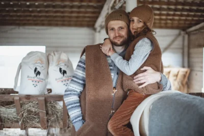 Ojciec z synem w szopce. Obydwaj w wełnianych kamizelkach. Chłopiec przytula Tatę. W tle worki z produktami Royal Alpaca.