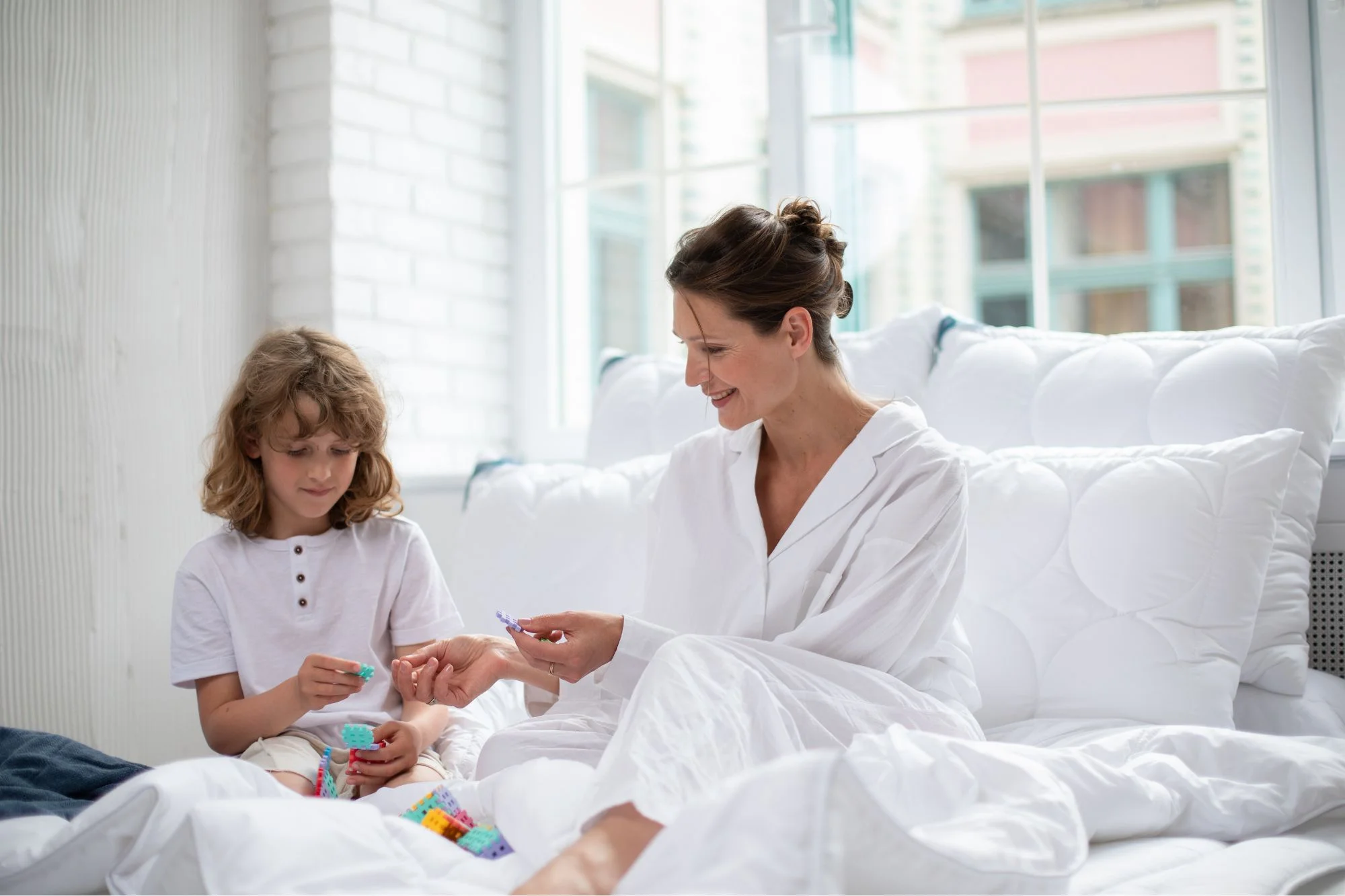 Kobieta i chłopiec bawią się na łóżku. Na łóżku kołdra i poduszki antyalergiczne.