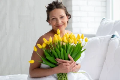 Kobieta w białej pościeli, trzyma bukiet różowych tulipanów