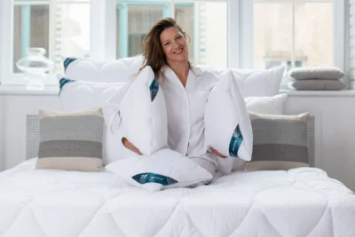 Kobieta siedząca na łóżku z kołdrą i poduszkami antyalergicznymi