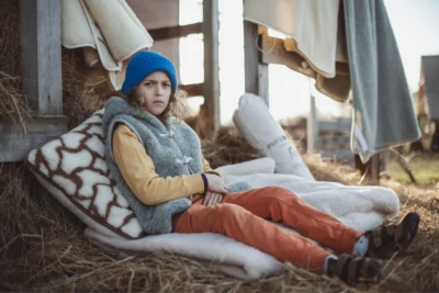 Chłopiec w wełnianej kamizelce siedzi na sianku, na wełnianym kocu, podparty poduszką wełnianą.