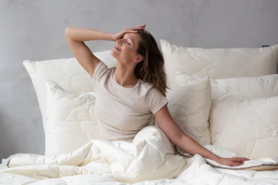 Kobieta siedzi na łóżku zawinięta w kołdrę z wełny merino