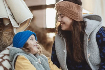 Kobieta z synem, ubrani w kamizelki wełniane, śmieją się.