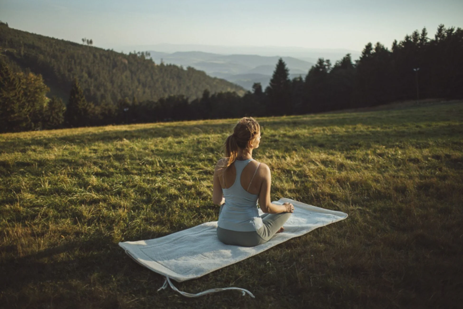 Kobieta praktykująca jogę na łące. Siedzi na macie wełnianej