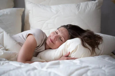 Kobieta leżąca na poduszce i pod kołdrą z wełny merynos.