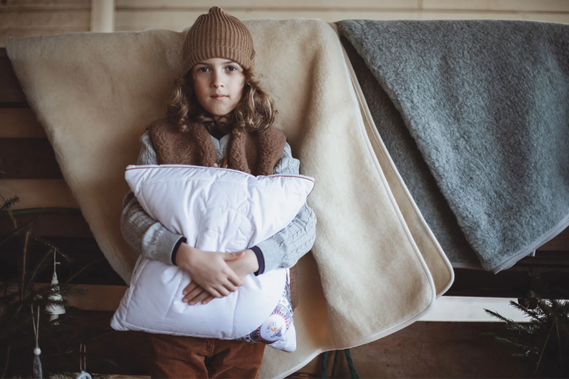 Chłopiec w wełnianej kamizelce, trzyma poduszkę. W tle wełniana kołdra i koc.