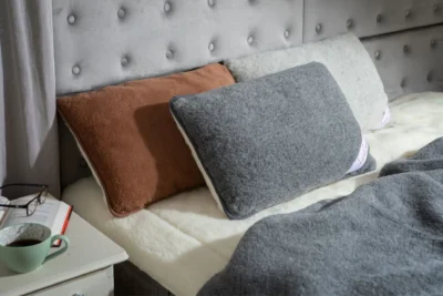 Łóżko, na nim kołdra i poduszki wełniane. Obok stolik nocny - na nim okulary, książka i kawa.