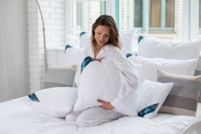 Kobieta siedząca w łóżku, trzyma poduszkę antyalergiczną.