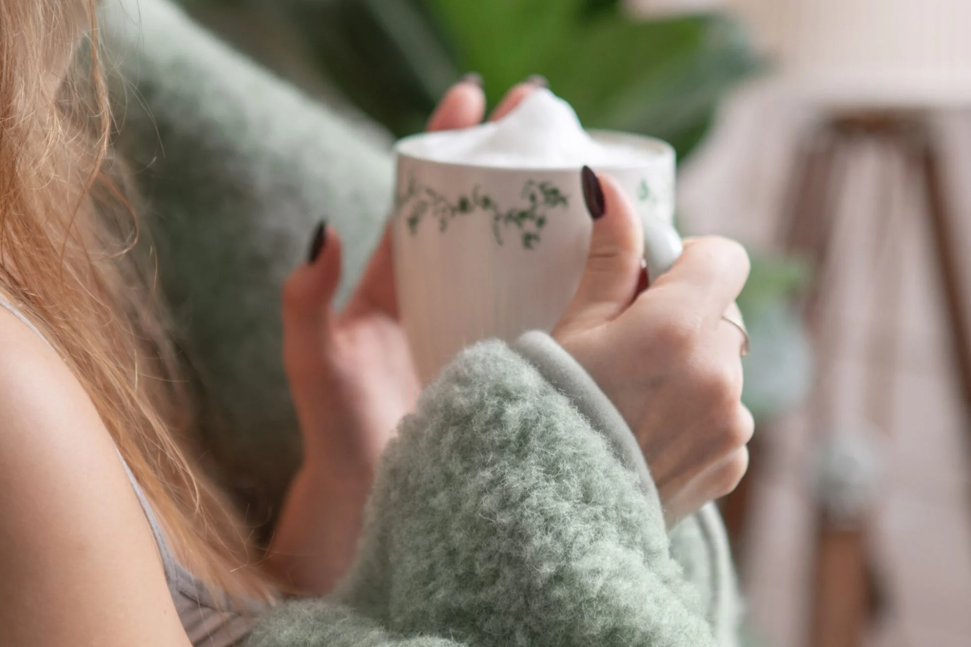 Kobieta owinięta kocem wełnianym, trzyma w dłoniach kubek z kawą