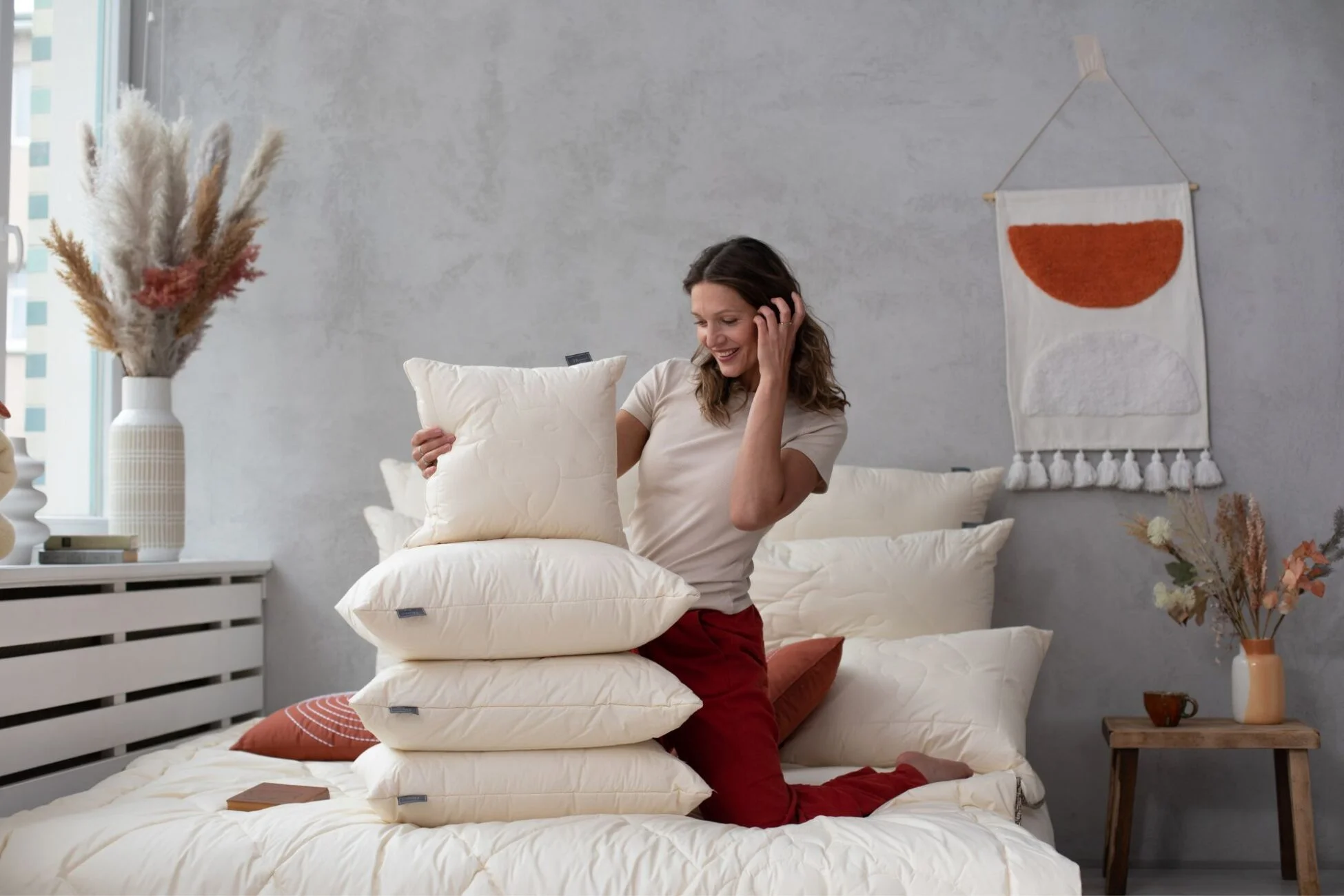 Kobieta klęcząca na łóżku, obok niej sterta poduszek z wełny merino
