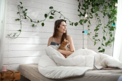 Kobieta siedząca pod kołdra, przytula rudego kota.