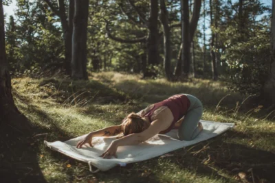 Kobieta praktykuje jogę na zewnątrz. Ćwiczy na macie wełnianej