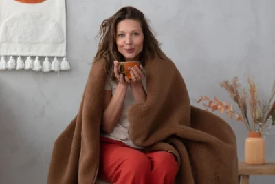 Kobieta owinięta wełnianym kocem merino pije herbatę