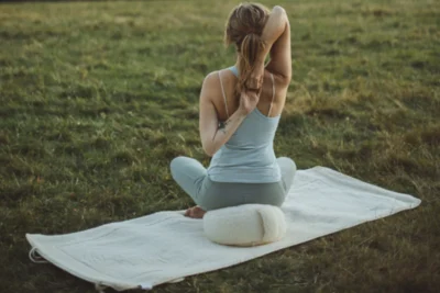 Kobieta praktykuje jogę na zewnątrz używając maty i poduszki do jogi