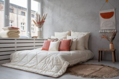 Sypialnia z łóżkiem z jasną pościelą, poduszkami w kolorze pomarańczowym i dywanem z juty