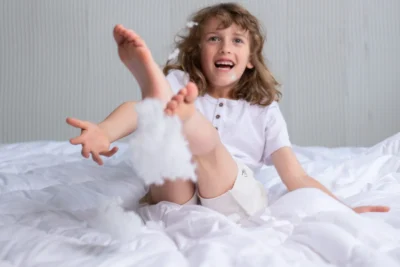 Uśmiechnięty chłopiec skacze po łóżku i rzuca wypełnieniem poduszki