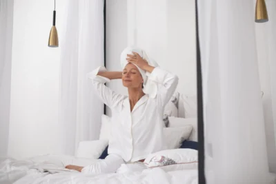 Kobieta w białej piżamie, przeciąga się z uśmiechem na łóżku