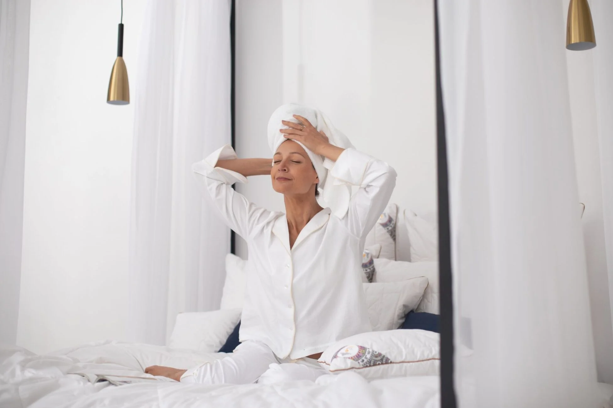 Kobieta w białej piżamie, przeciąga się z uśmiechem na łóżku