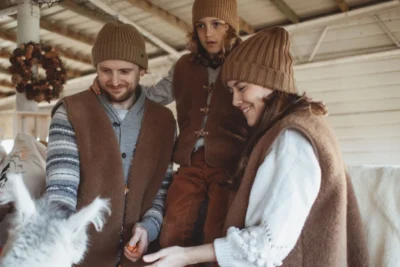 Rodzina ubrana w wełniane kamizelki karmi alpakę.