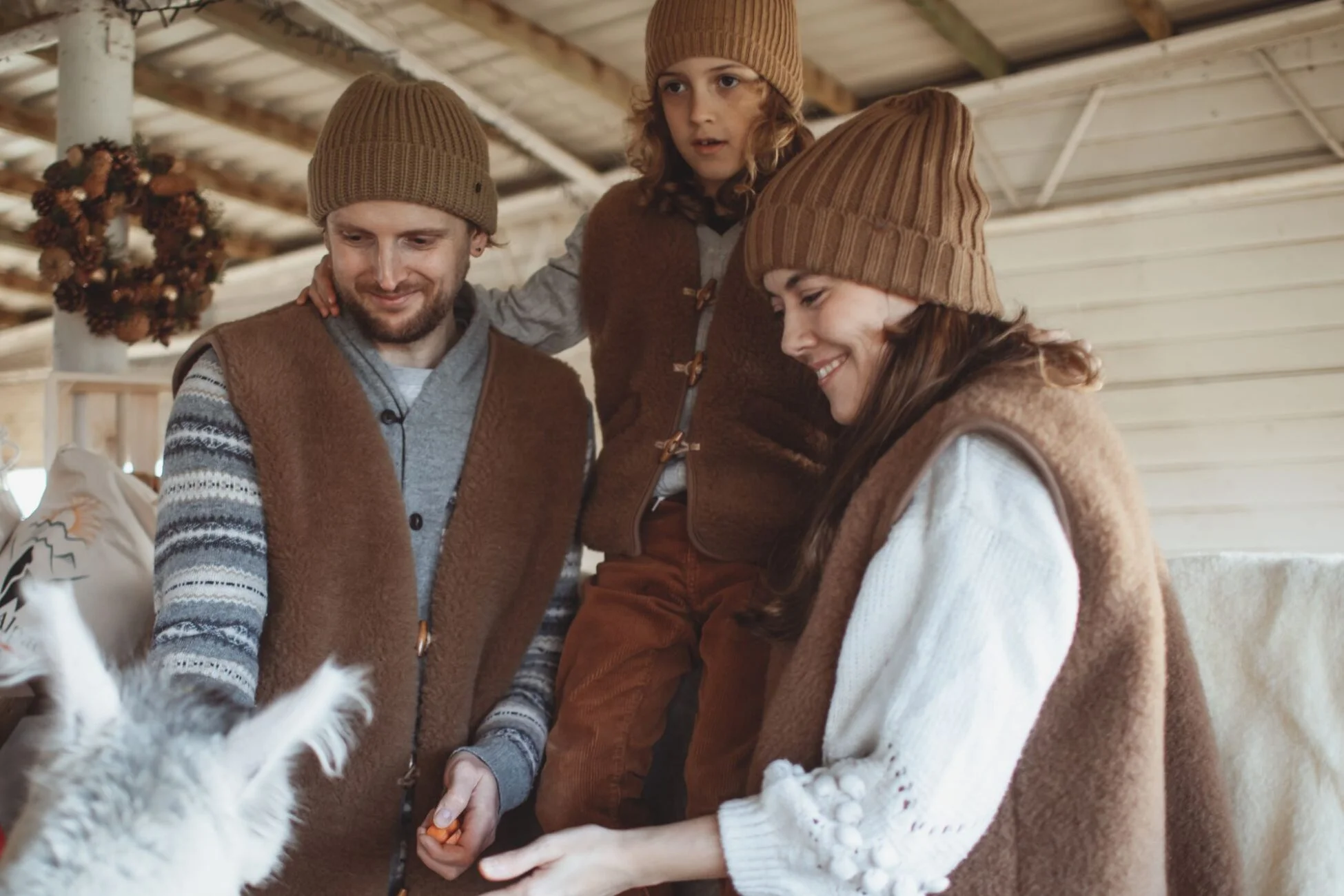 Rodzina ubrana w wełniane kamizelki karmi alpakę.