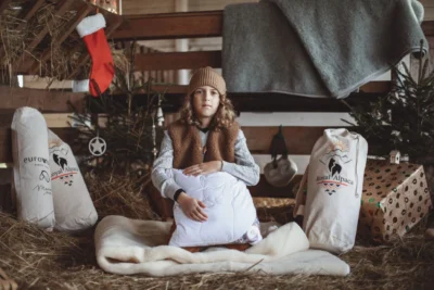 Chłopiec w kamizelce wełnianej, siedzi w stajence w świątecznej aranżacji