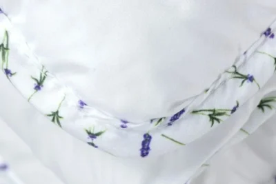 Zbliżenie na kołdrę lawendową. Kołdra jest biała, na lamówce wzór lawendy