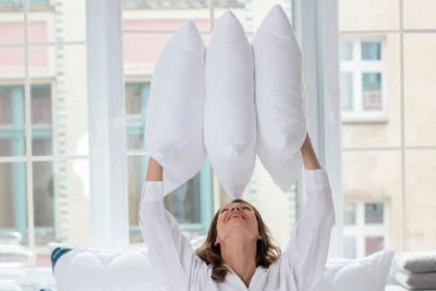 Uśmiechnięta kobieta, trzyma nad głową trzy białe poduszki z jonami srebra.