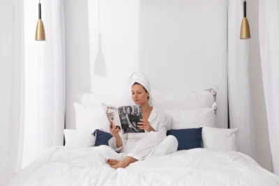 Kobieta siedząca w białej piżamie w pościeli z wełny alpaki (poduszki i kołdra), czyta książę.