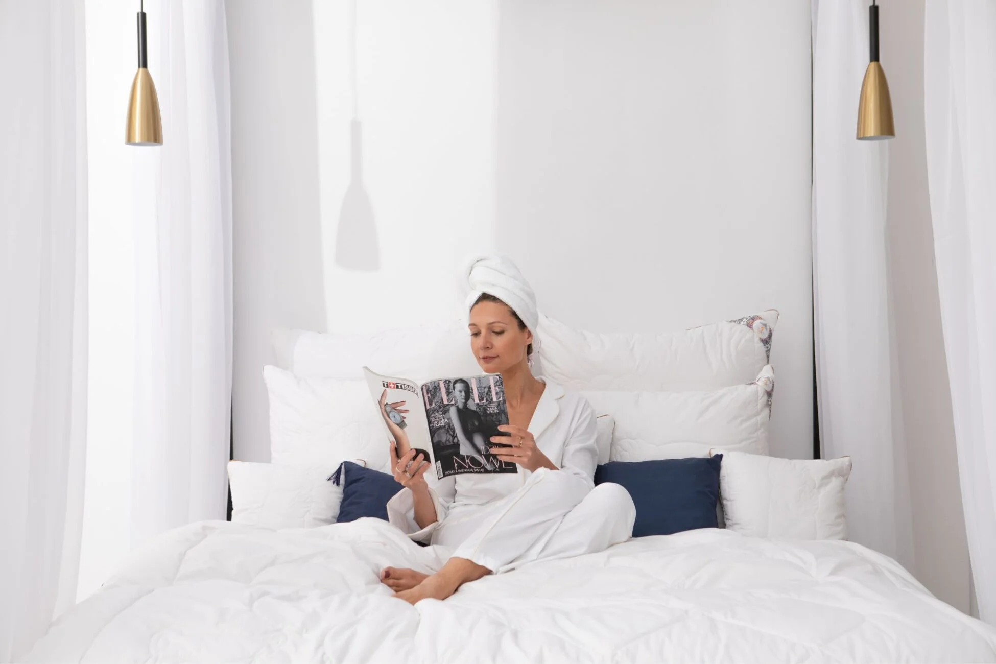 Kobieta siedząca w białej piżamie w pościeli z wełny alpaki (poduszki i kołdra), czyta książę.