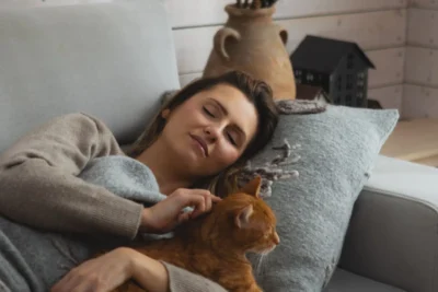 Kobieta drzemie owinięta w koc wełniany polskiego producenta Eurowolle. Przytula rudego kota.