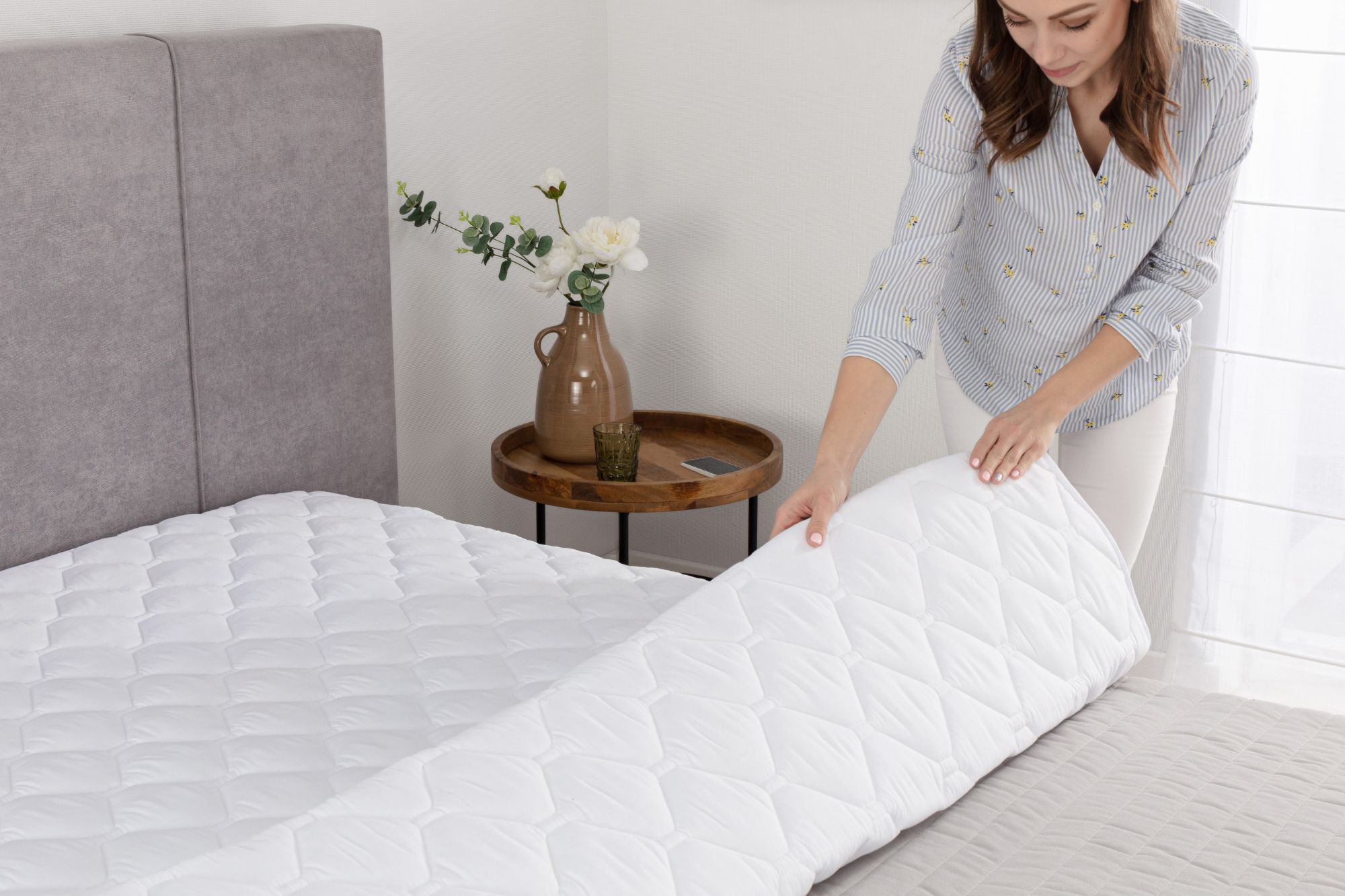 Kobieta zakłada podkład pod prześcieradło na materac.