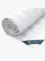 biały ochraniacz na materac antyalergiczny zawinięty w rolkę na neutralnym tle