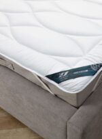 Ochraniacz w kolorze białym na materacu na szarej kanapie