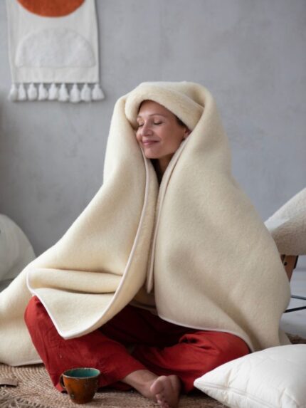 Kobieta siedząca w wełnianym kocu w jasnym kolorze, relaksująca się w przytulnym wnętrzu