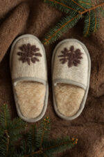 wełniane kapcie w beżowym kolorze ze wzorem brązowej gwiazdki, na brązowym tle z gałązką świerku