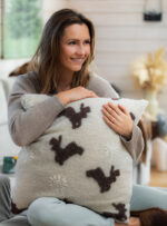 Kobieta trzyma poduszkę z wełny z motywem jelonków i gwiazdek w jasnym wnętrzu