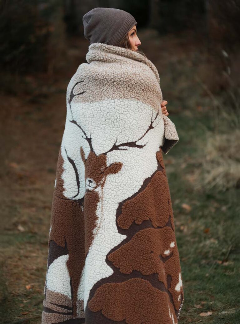 Kobieta owinięta w brązowy koc z wzorem na tle natury