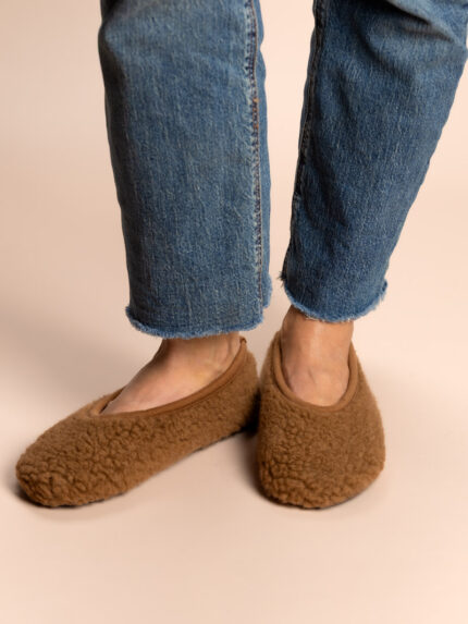Vollbraune Wollhausschuhe an den Füßen, Jeans, neutraler Hintergrund