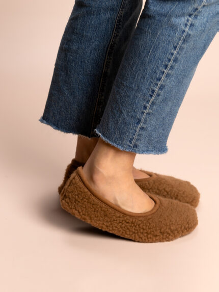 Vollbraune Hausschuhe an den Füßen, Jeans mit ausgewaschenen Hosenbeinen, neutraler Hintergrund