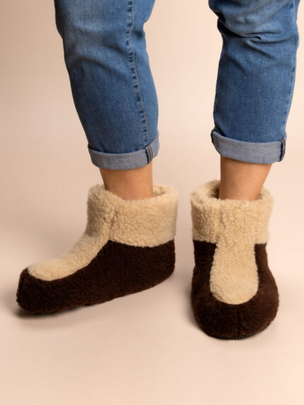 wysokie wełniane kapcie w kolorze brązowym i beżowym na stopach osoby w dżinsach