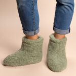 wysokie jasno zielone kapcie z wełny na stopach osoby w niebieskich spodniach na jasnym tle